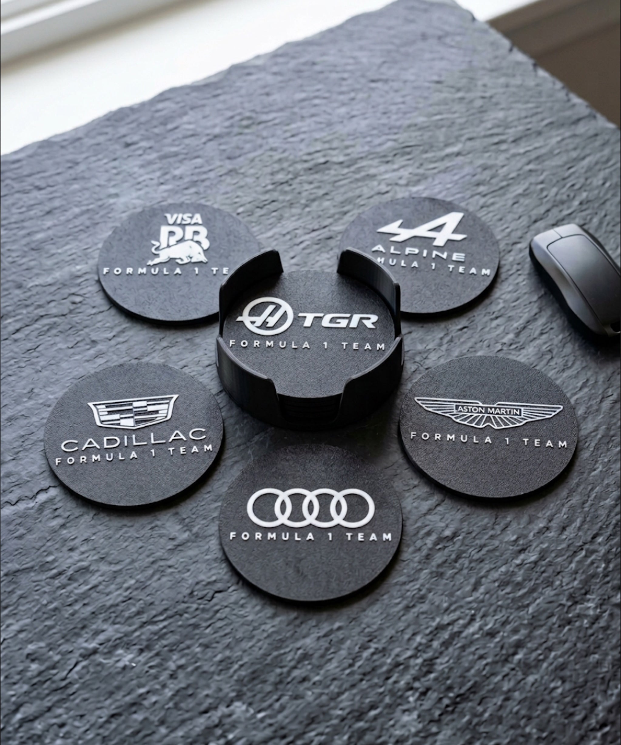 Close-up of Formula 1 team logo coasters set with 3D printed holder on textured surface